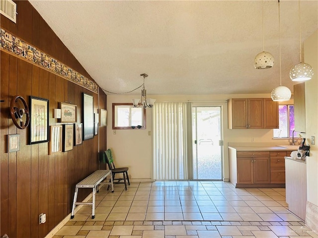 kitchen featuring wooden walls, decorative light fixtures, plenty of natural light, and lofted ceiling