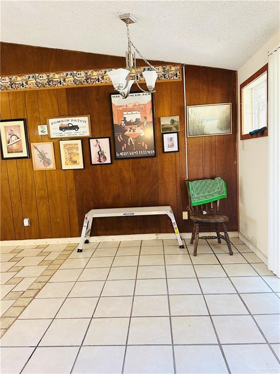 unfurnished dining area with a textured ceiling, vaulted ceiling, wooden walls, tile patterned flooring, and a chandelier