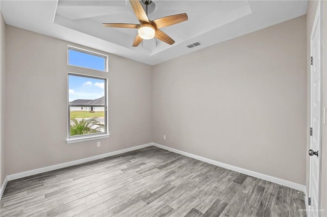 unfurnished room featuring ceiling fan, light wood-type flooring, and a tray ceiling