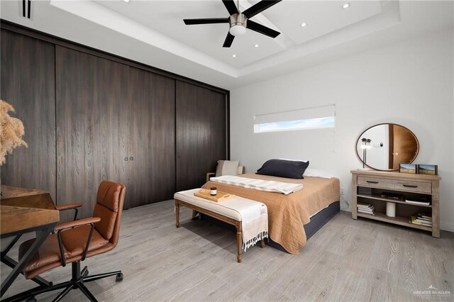 bedroom with ceiling fan, a raised ceiling, and light hardwood / wood-style flooring