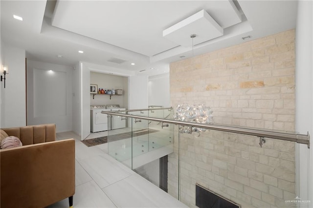 hallway with a raised ceiling, light tile patterned floors, tile walls, and washing machine and clothes dryer