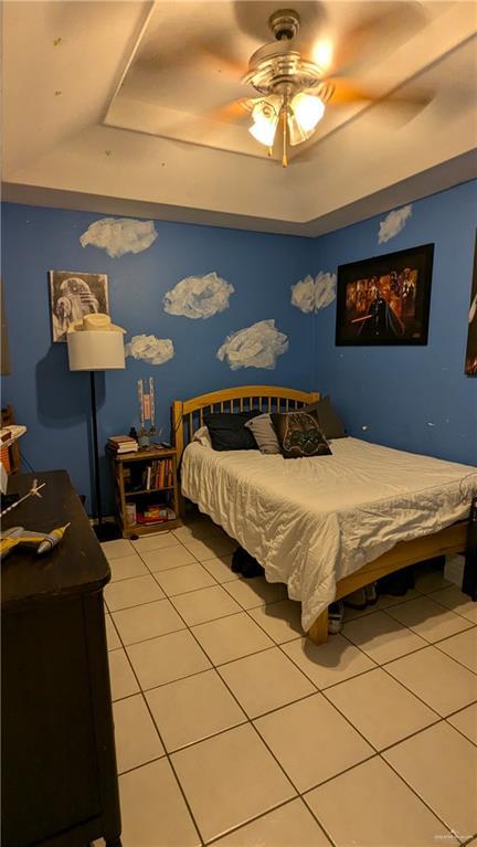 bedroom with tile patterned flooring, a tray ceiling, and ceiling fan