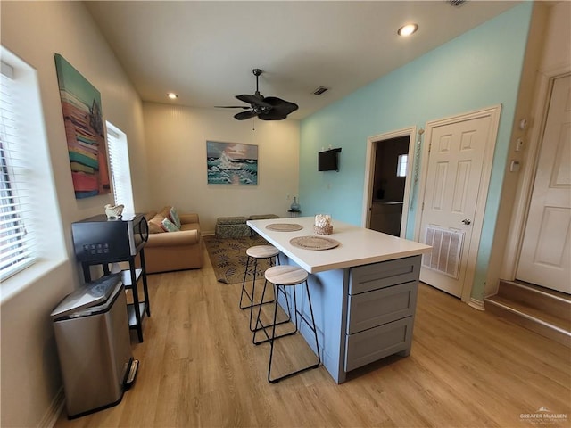 kitchen featuring light wood-type flooring, a center island, gray cabinets, ceiling fan, and a breakfast bar area