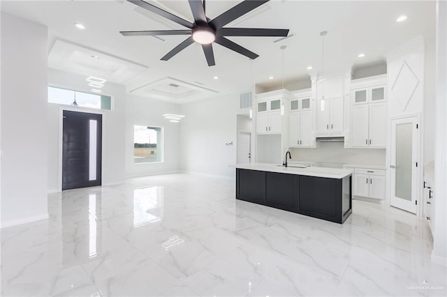 kitchen with sink, an island with sink, hanging light fixtures, and white cabinets