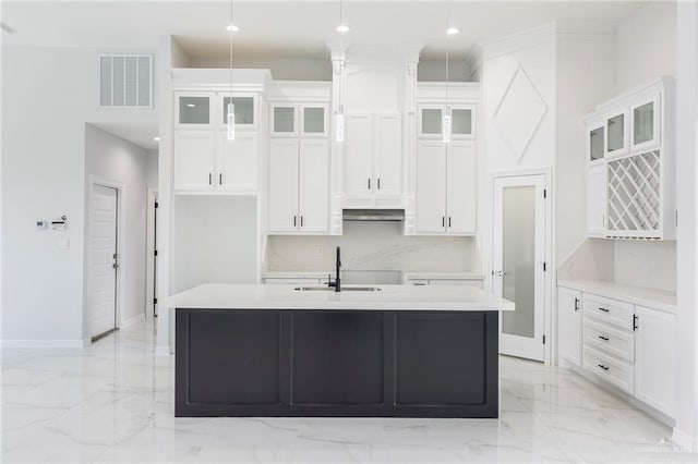 kitchen with white cabinetry, hanging light fixtures, sink, and a center island with sink