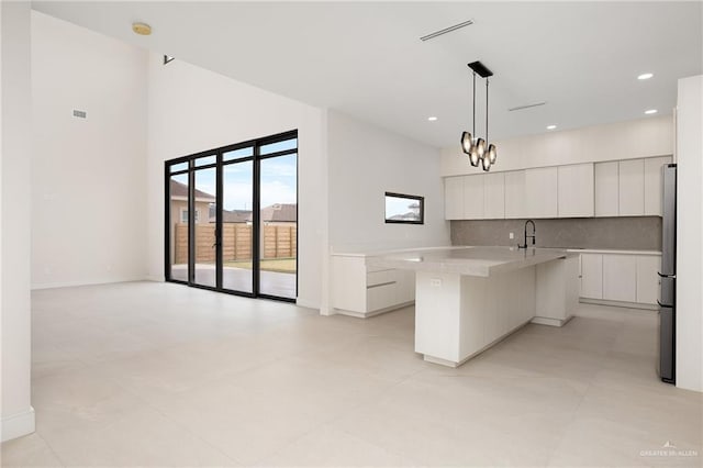 kitchen featuring white cabinetry, backsplash, hanging light fixtures, and an island with sink