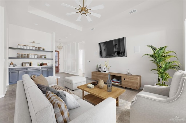 living area with a dry bar, visible vents, a raised ceiling, ceiling fan, and light wood-type flooring