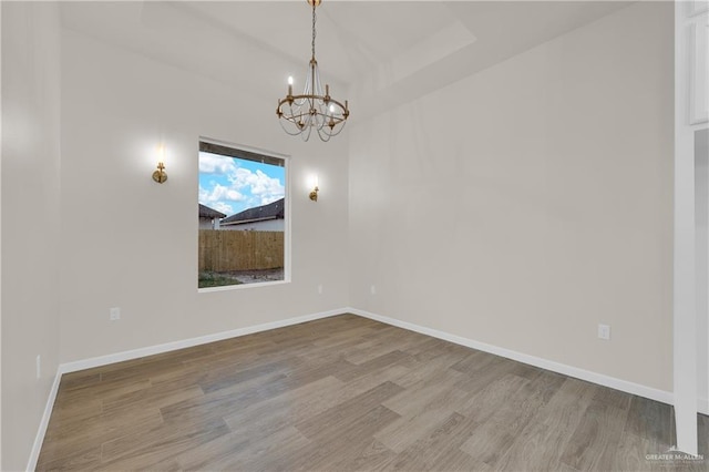 spare room with baseboards, a chandelier, and wood finished floors