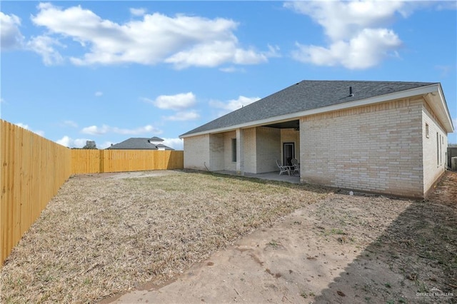 back of house with a fenced backyard, central AC, brick siding, roof with shingles, and a patio area