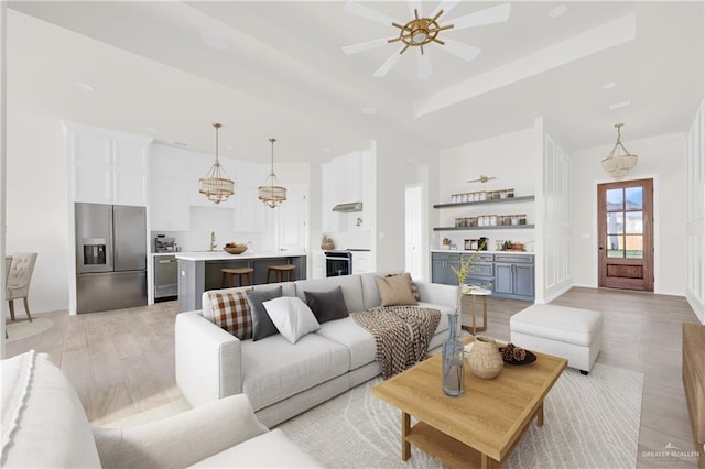 living room featuring a raised ceiling, ceiling fan, and light wood-style flooring