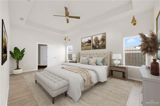 bedroom featuring ceiling fan, light wood-style flooring, visible vents, baseboards, and a tray ceiling