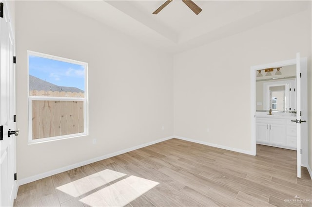 unfurnished bedroom featuring a raised ceiling, connected bathroom, ceiling fan, light wood-type flooring, and baseboards