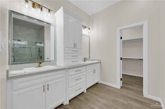 full bath with wood finished floors, a sink, a marble finish shower, and a walk in closet