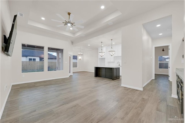 unfurnished living room featuring light wood finished floors, a tray ceiling, ceiling fan with notable chandelier, and visible vents