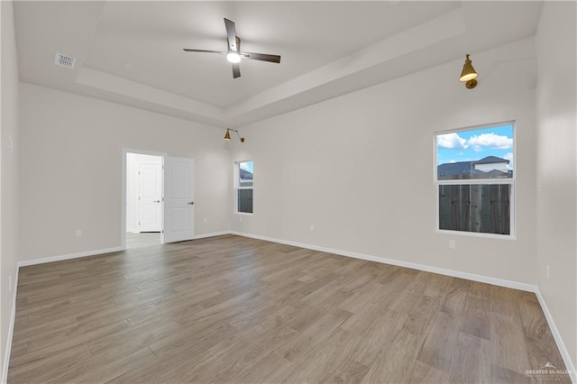 spare room featuring light wood finished floors, baseboards, and a tray ceiling