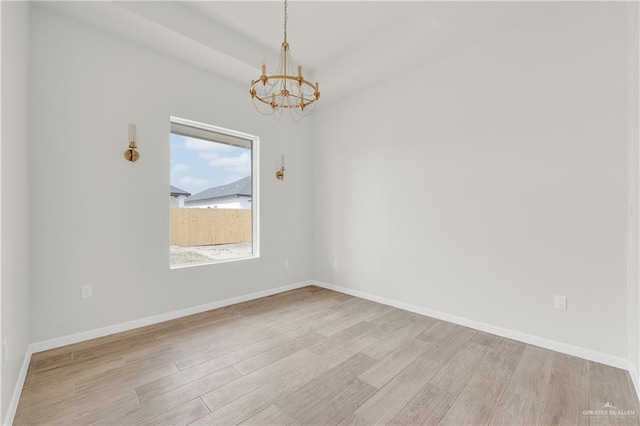 empty room featuring light wood-type flooring, an inviting chandelier, and baseboards