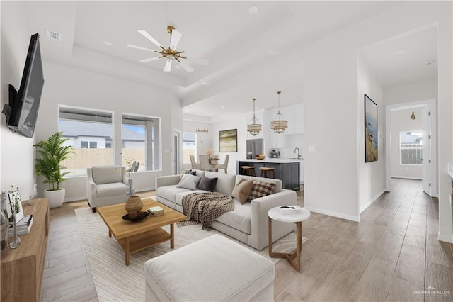 living area with visible vents, baseboards, ceiling fan, a tray ceiling, and light wood-style floors