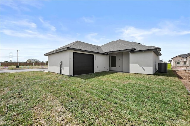 rear view of house with a yard, stucco siding, central AC unit, fence, and a garage