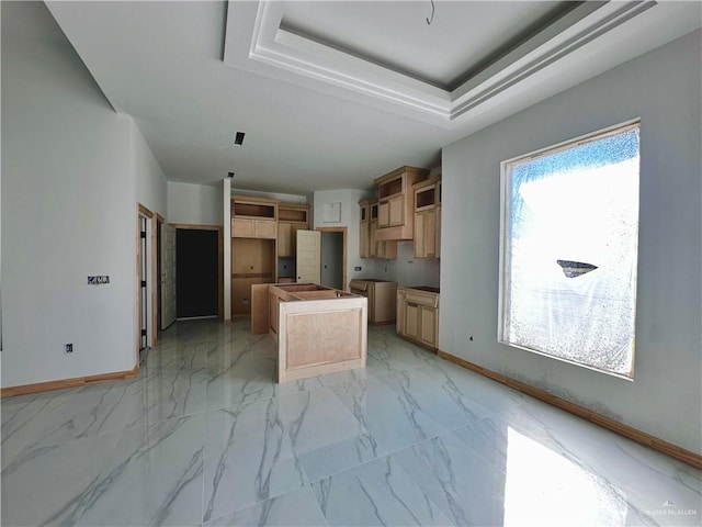 kitchen featuring marble finish floor, baseboards, a kitchen island, and a tray ceiling