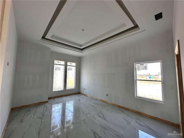 empty room featuring marble finish floor, baseboards, and a tray ceiling