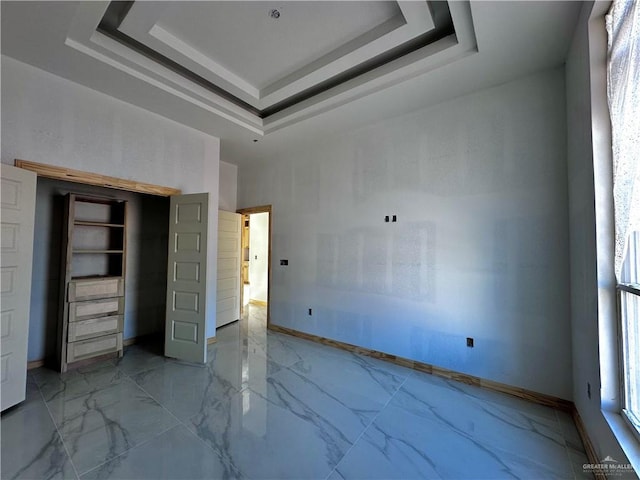 unfurnished bedroom featuring marble finish floor, baseboards, and a raised ceiling