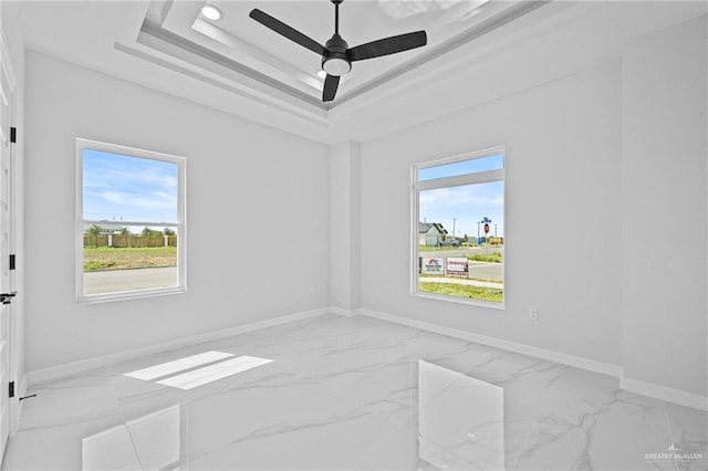 unfurnished room featuring a raised ceiling, ceiling fan, marble finish floor, and baseboards