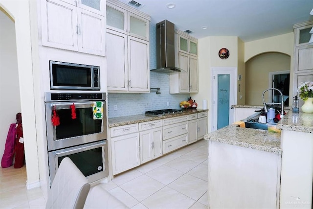 kitchen featuring light stone counters, light tile patterned flooring, stainless steel appliances, and wall chimney range hood