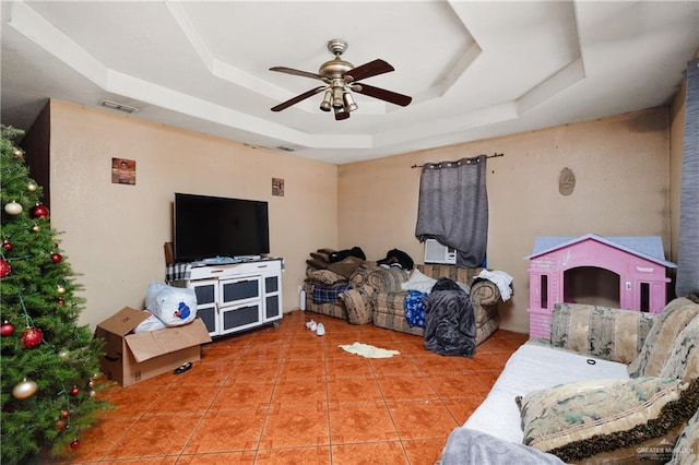 living area with ceiling fan, a tray ceiling, tile patterned flooring, and visible vents