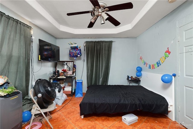 bedroom with ceiling fan, a tray ceiling, and tile patterned floors