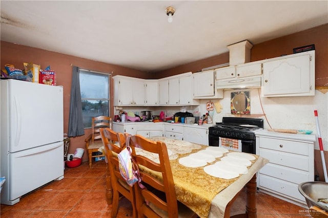 kitchen with white cabinets, black gas range oven, freestanding refrigerator, light countertops, and under cabinet range hood