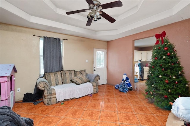 living area featuring light tile patterned floors, a tray ceiling, and a ceiling fan