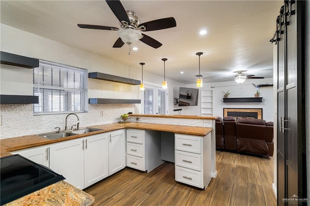 kitchen with sink, dark wood-type flooring, white cabinetry, hanging light fixtures, and kitchen peninsula