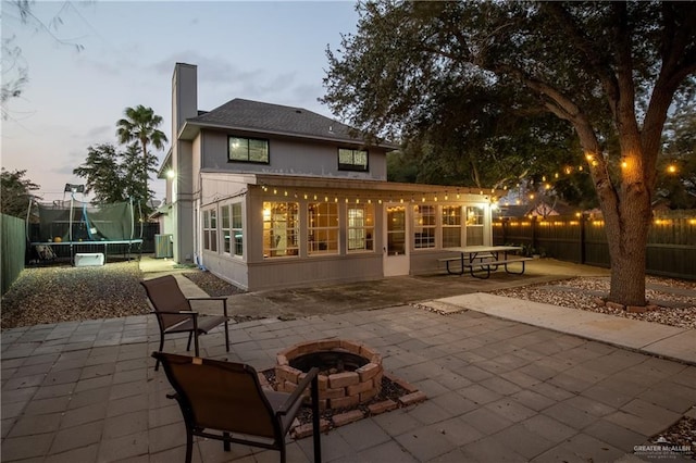 back house at dusk featuring a patio, cooling unit, a trampoline, and an outdoor fire pit