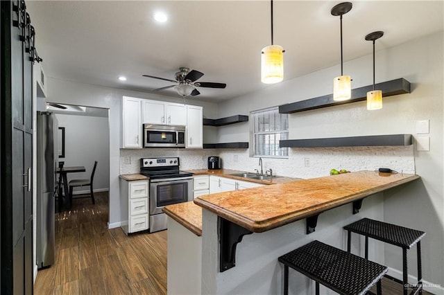 kitchen featuring pendant lighting, stainless steel appliances, kitchen peninsula, and white cabinets