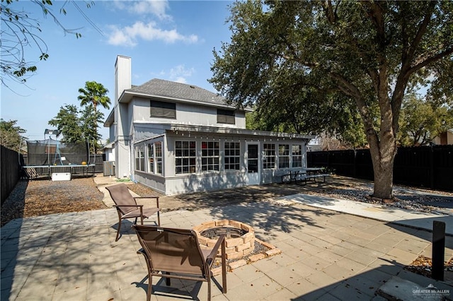 rear view of property with a trampoline, a sunroom, a patio area, and a fire pit