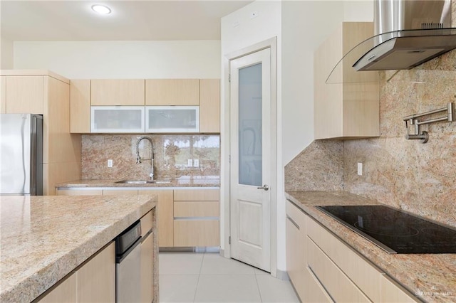 kitchen featuring wall chimney range hood, light brown cabinetry, and freestanding refrigerator