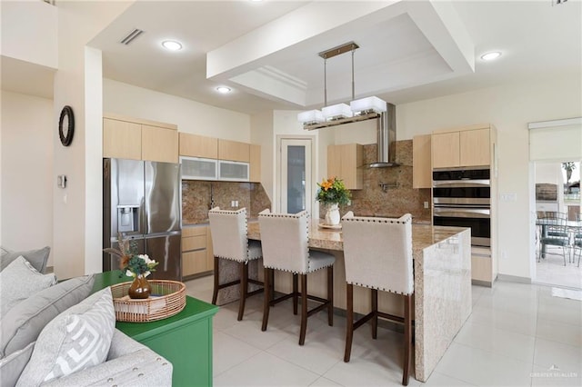 kitchen featuring visible vents, a raised ceiling, wall chimney exhaust hood, appliances with stainless steel finishes, and light brown cabinetry