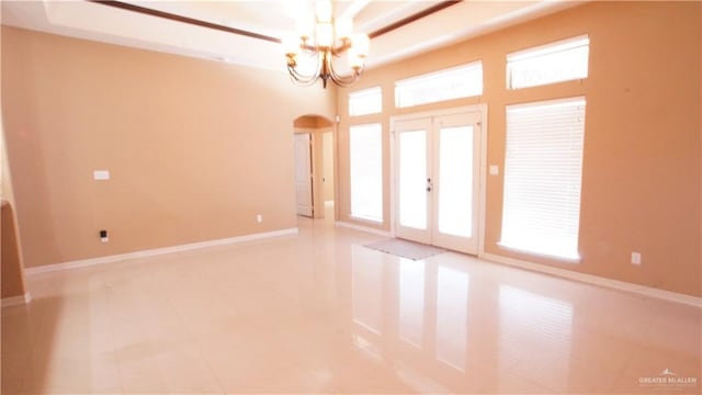 unfurnished room featuring a chandelier, a raised ceiling, and french doors