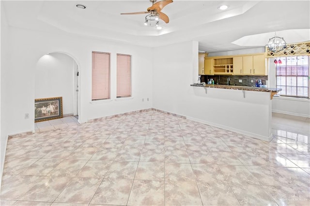 unfurnished living room featuring a tray ceiling, ceiling fan, and light tile patterned floors