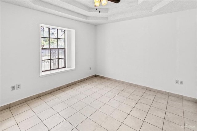 spare room featuring a textured ceiling, a raised ceiling, ceiling fan, and light tile patterned flooring