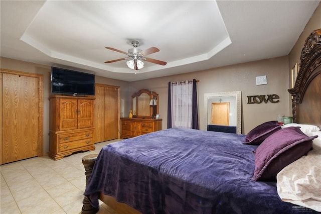 tiled bedroom with ceiling fan and a tray ceiling