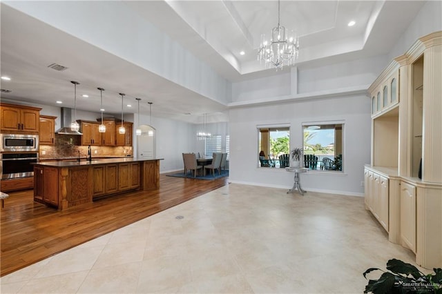 kitchen with appliances with stainless steel finishes, wall chimney exhaust hood, an inviting chandelier, light hardwood / wood-style flooring, and hanging light fixtures