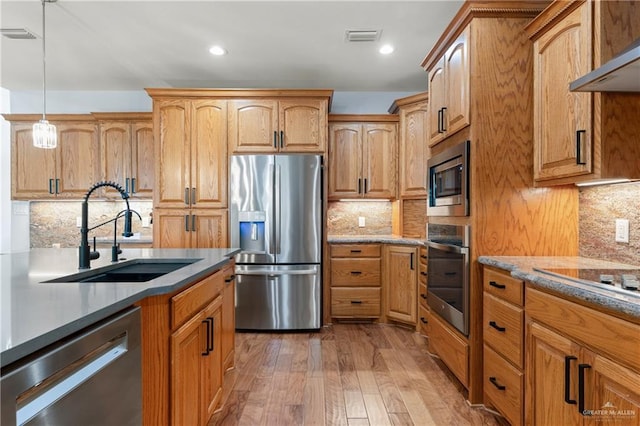 kitchen with appliances with stainless steel finishes, light wood-type flooring, ventilation hood, sink, and decorative light fixtures