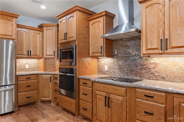 kitchen with backsplash, stainless steel appliances, light hardwood / wood-style floors, and wall chimney range hood