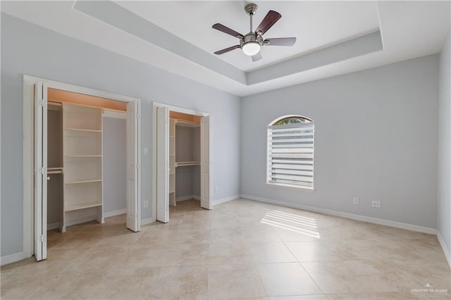 unfurnished bedroom featuring a tray ceiling, a walk in closet, ceiling fan, and light tile patterned flooring