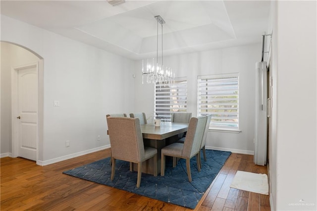 dining space with hardwood / wood-style flooring, a chandelier, and a tray ceiling