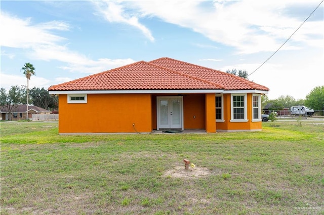 back of house with a tile roof, a lawn, and stucco siding