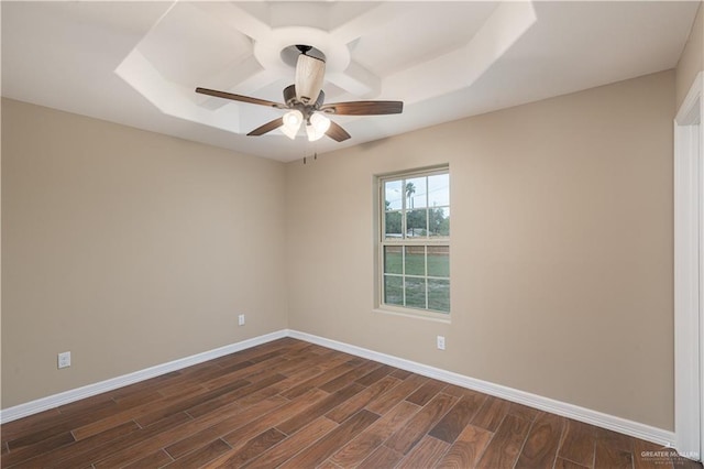 spare room with dark wood-style flooring, a raised ceiling, ceiling fan, and baseboards