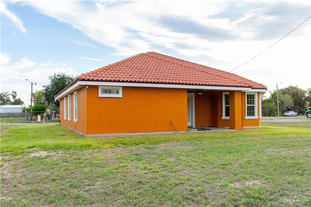 back of property featuring a lawn, fence, a tile roof, and stucco siding