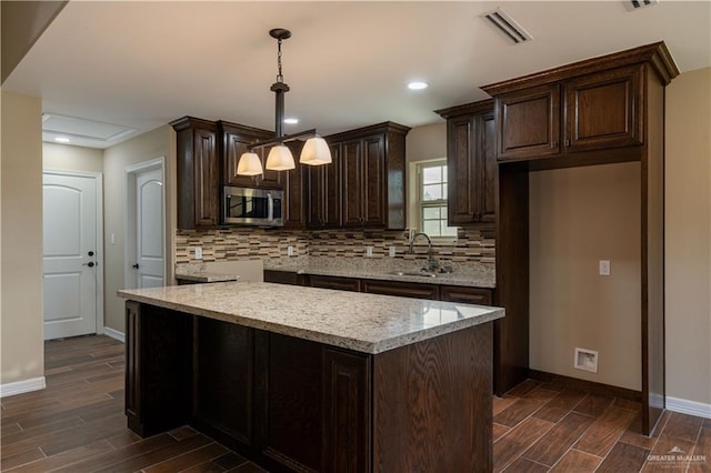 kitchen featuring decorative backsplash, stainless steel microwave, wood tiled floor, dark brown cabinets, and a sink